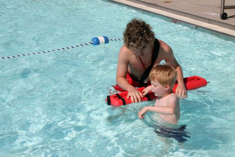 Photo shows lifeguard helping boy in pool at Water Safety Day.