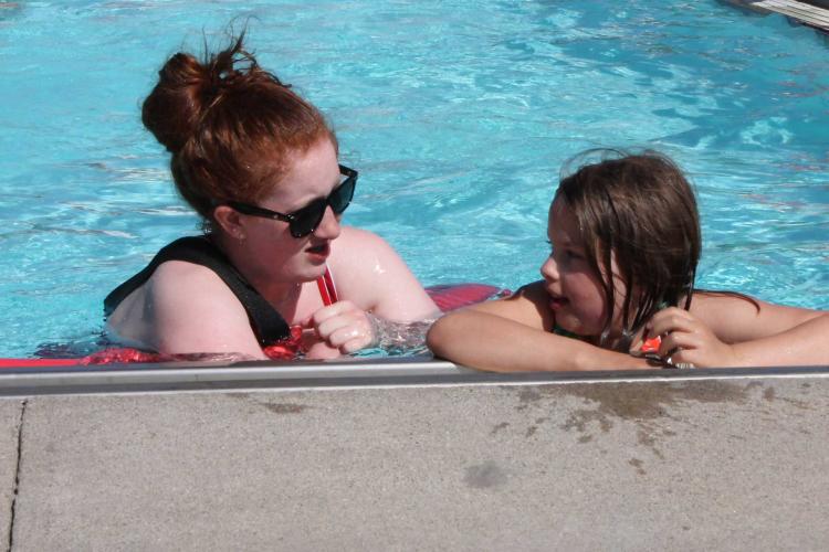 Photo shows lifeguard talking to girl in pool at Water Safety Day.
