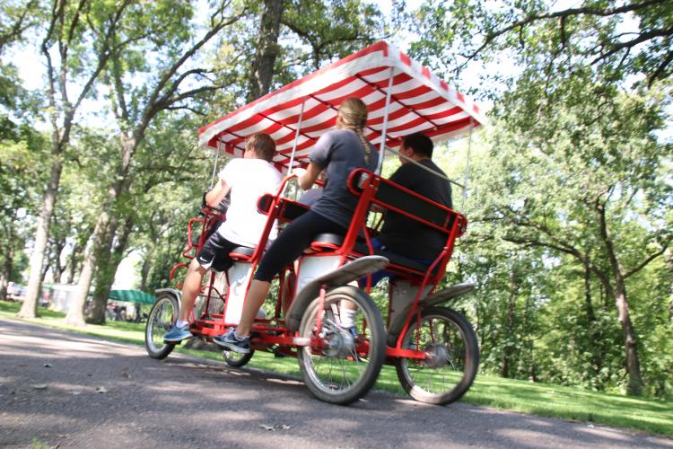 This image shows a group of four people riding a single surrey bike at Lindenwood Park.