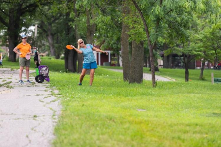 This image shows two females, one about to throw her frisbee at a disc golf tournament.