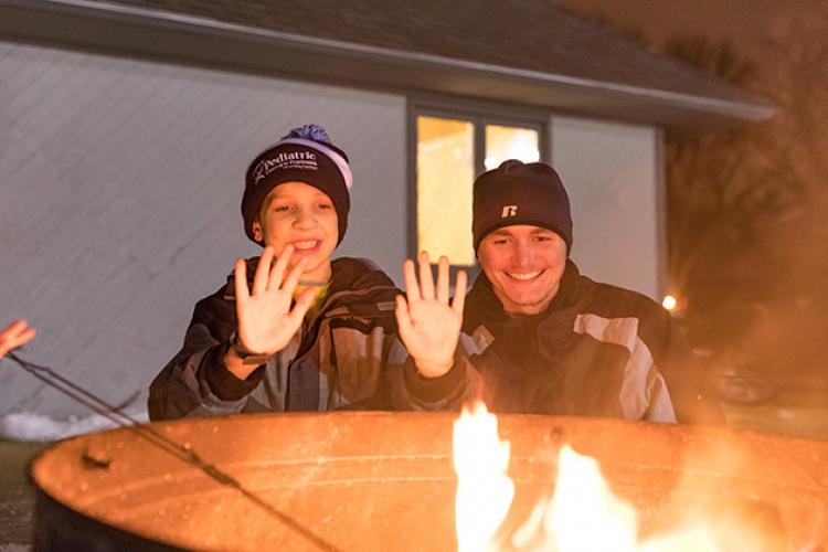 This image shows an adult and child warming up by a firepit at S'mores and More.