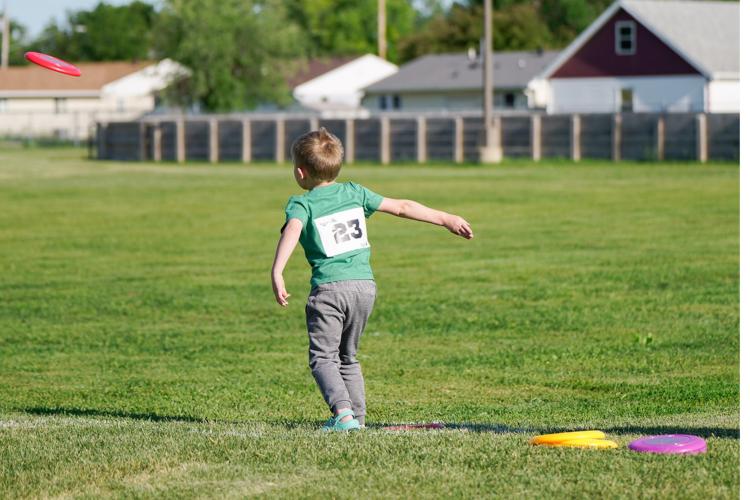Kids Triathlon - Frisbee Throw kid in grass field with participant number bib on throwing a frisbee