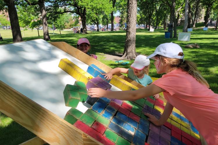 three hids in hats and painted faces playing large scale colorful tetris in island park
