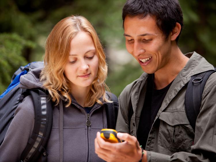Geocaching Team A woman and man looking at a GPD device in backpacks in park