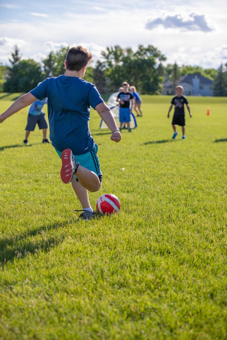 Boy kicking soccer ball in park into 3 boys waiting