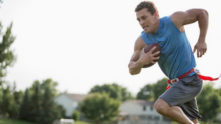 Adult Flag Football Man in the act of running with football in arm outside in a park playing flag football