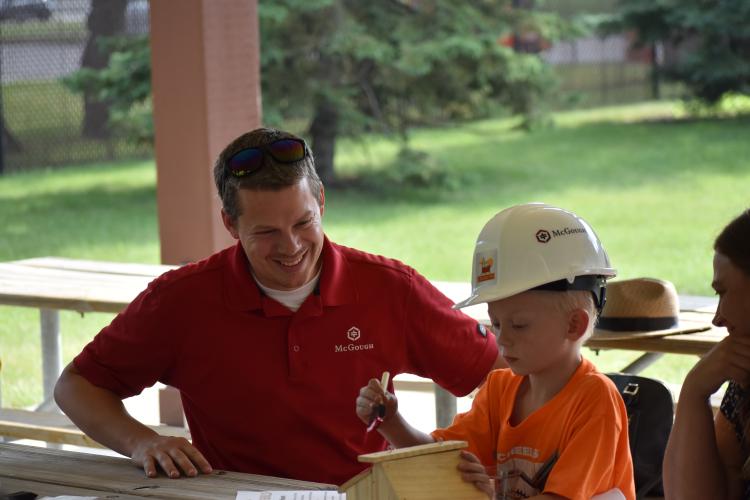Male McGough staff sitting at picnic table helping boy sitting next to him put together a wooden bird house.