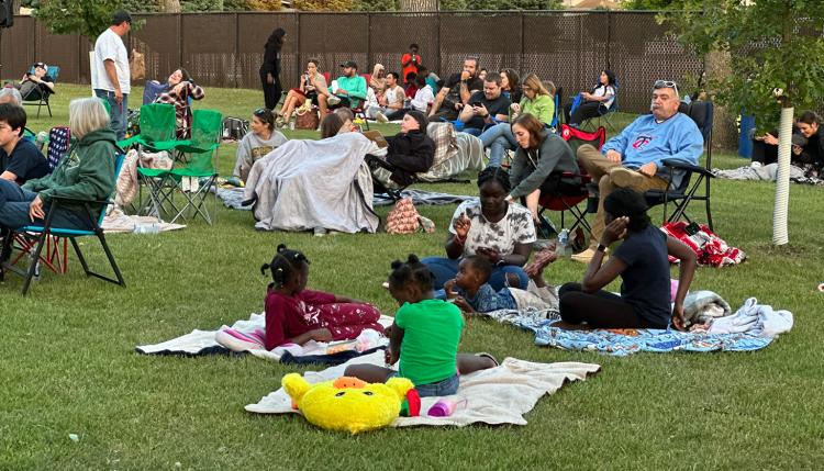 20+ people sit on the lawn in folding chairs or on blankets waiting for the Movie in the Park movie to start at Rheault Farm