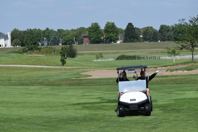 two men waving from a golf cart on a golf course