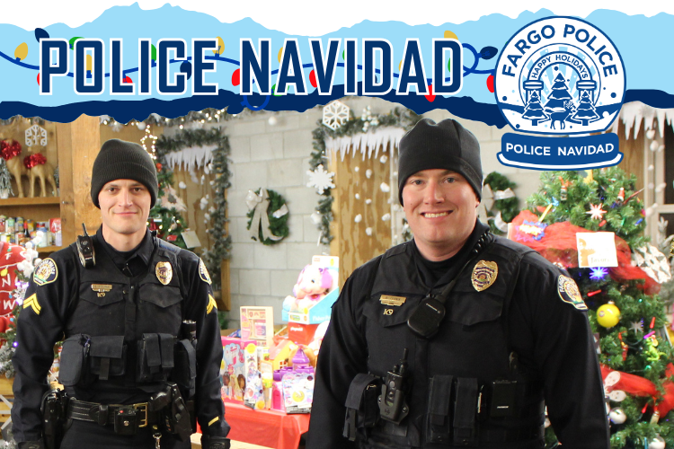 Two Policemen standing in the Santa Village barn with loads of donated gifts and food. POLICE NAVIDAD above the men and the Fargo Police snow globe