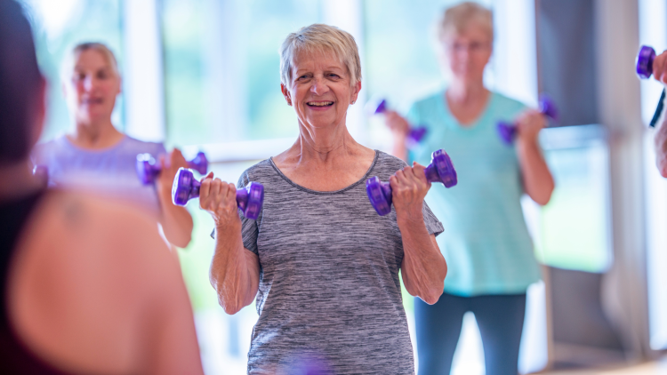 Active Agers Program.png Senior woman lifting dumbbells in a group workout class.