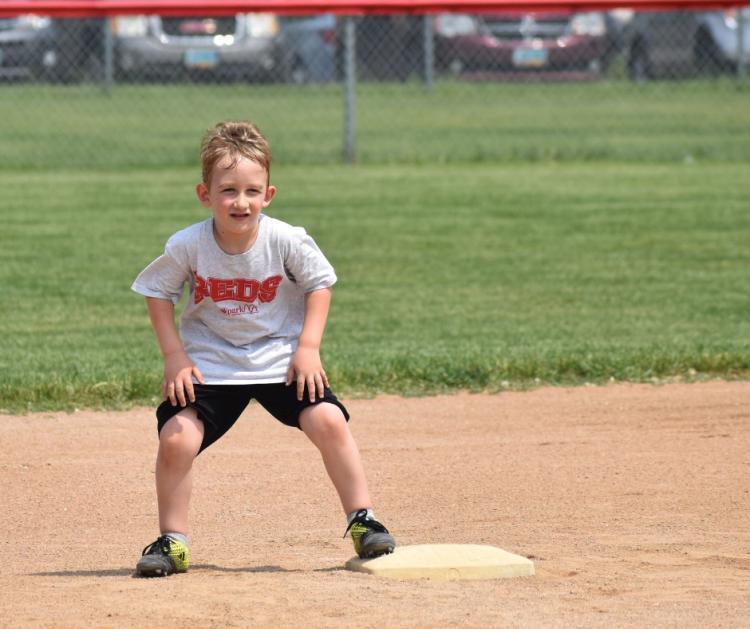 Young boy leading off the base on a baseball field outside on a beautiful day.