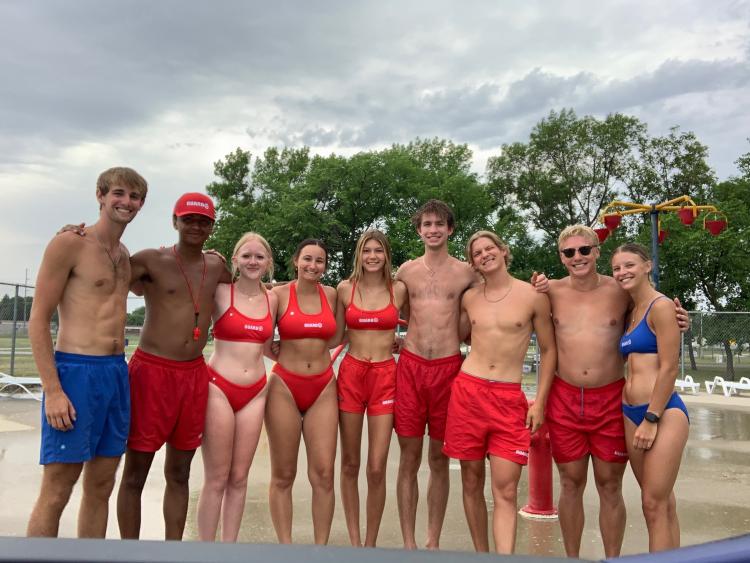 9 lifeguards at the Madison Outdoor Pool standing together lined up for a picture.