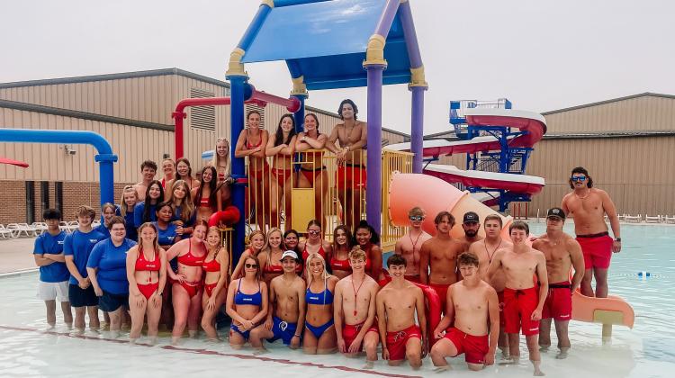 Lifeguards at the South High Outdoor Pool standing on the aquatic playground lined up for a picture.