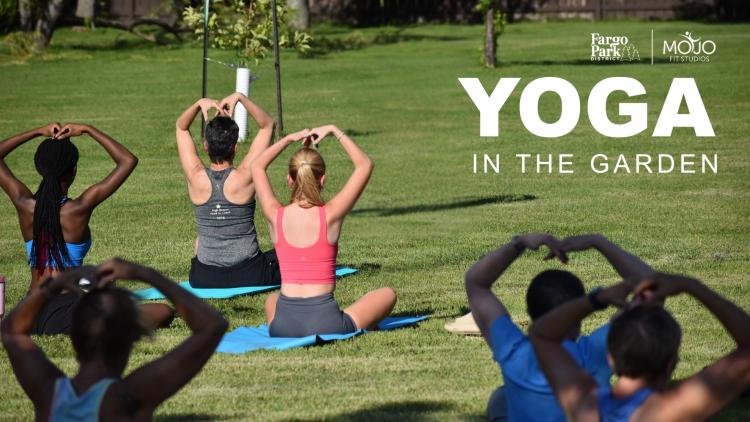 6 adults sitting on yoga mats outside in a green space participating in a group yoga session