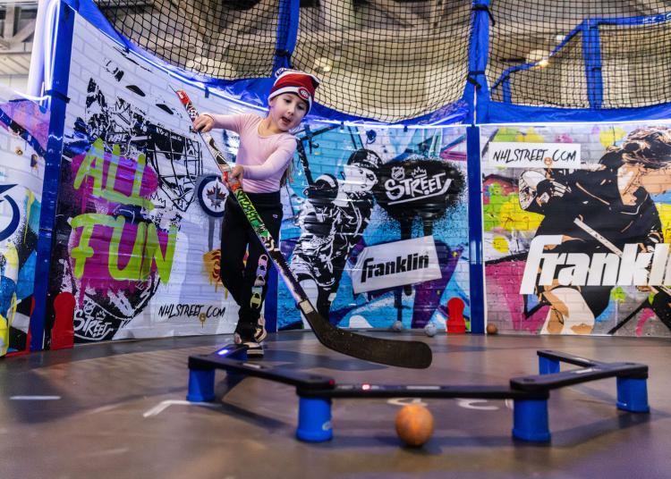 Child practicing stick handling with colorful boards behind her on concrete floor