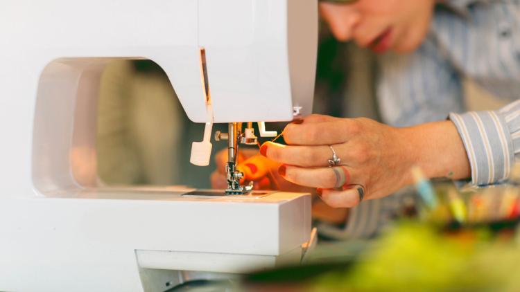 Adult Sewing Close-up of a person threading a sewing machine needle, with their face partially visible in the background and sewing tools blurred in the foreground.