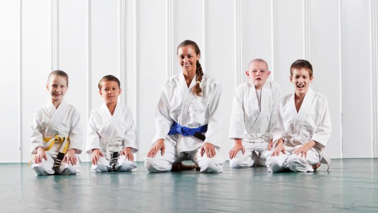 4 kids in Jiu Jitsu robes with an instructor in her robe in front of a white wall