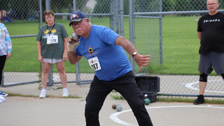 This image shows a senior athlete preparing to throw a shot put during the North Dakota Senior Games track and field event.