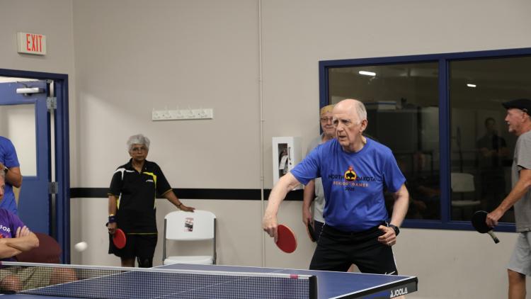 This image shows senior athletes playing table tennis indoors during the North Dakota Senior Games.