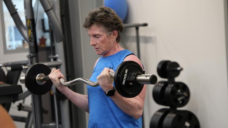 This image shows a woman lifting a barbell while strength training during the North Dakota Senior Games.