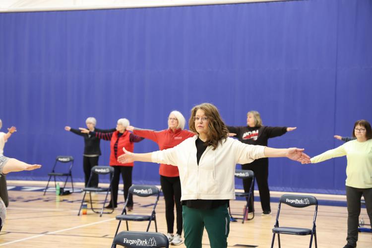 adults 55+ standing in gym with chair next to each stretching for the SAIL program