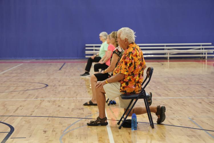 adults 55+ sitting in gym on a chair stretching for the SAIL program