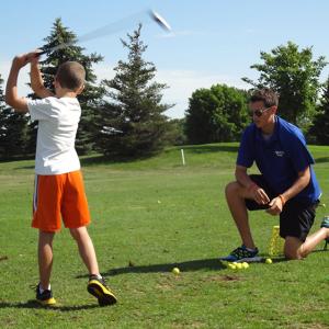 This image shows the coach helping a boy during youth golf lessons.