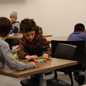 Children sit at tables building with LEGO® bricks during an indoor youth recreation program.