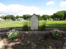 Roosevelt Park signage in behind 2 flowering bushes.  Sign in front of open field