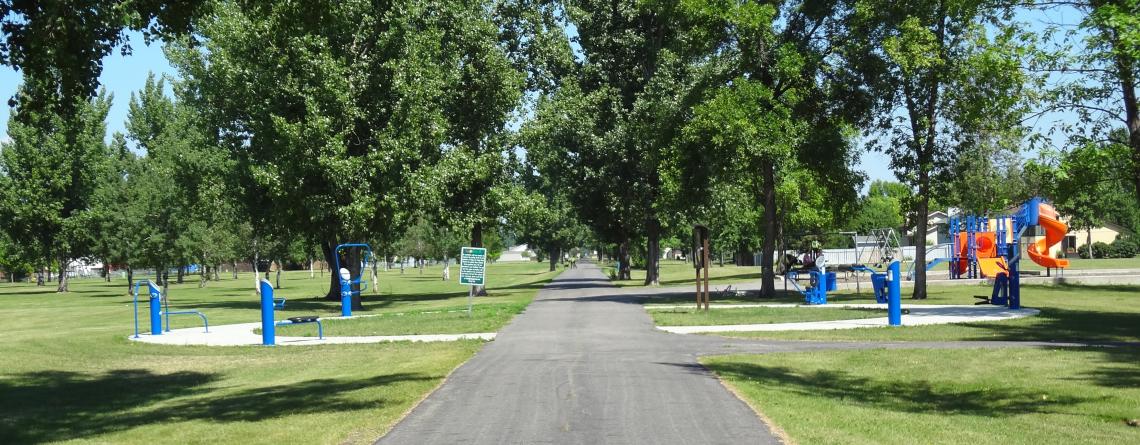 This image shows the exercise equipment with the playground in the background at Milwaukee Trail North Park.