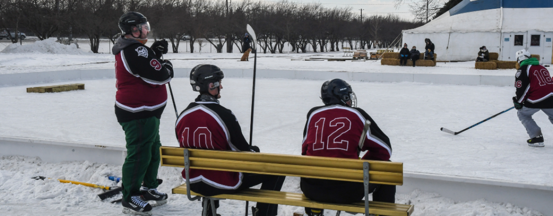 three men sitting on bench outside pond hockey rink