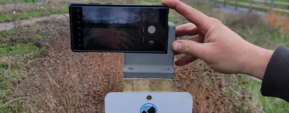 Photo of a phone taking a picture of Orchard glen park on a chronolog photo station