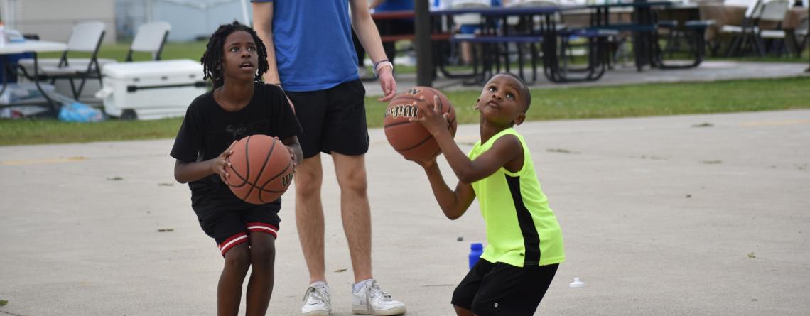 Two kids playing basketball on an outdoor basketball court in the park.