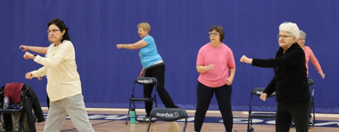 6 older women in a gym doing light exercise.