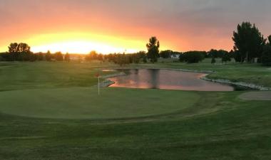 sun setting over putting green with red flag and water hazard on right side