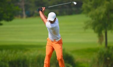 A young man golfing on a green course wearing orange pants and a white shirt and hat