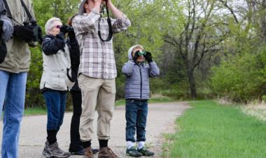5 people standing in a forest looking through binoculars.