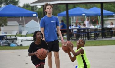 Two kids playing basketball on an outdoor basketball court in the park.