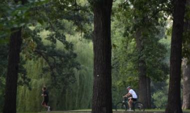 Person jogging and another person riding a bicycle along a paved trail through a wooded Fargo park.