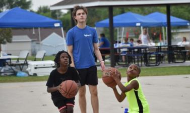 Two kids playing basketball on an outdoor basketball court in the park.