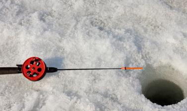 Photo of an ice fishing pole next to an ice fishing hole in the ice