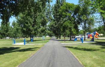 This image shows the exercise equipment with the playground in the background at Milwaukee Trail North Park.