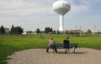 This image shows two people on a bench at the Village West Dog Park.