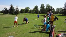 This image shows the coach demonstrating while the group of kids watch during youth golf lessons.
