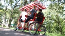 This image shows a group of four people riding a single surrey bike at Lindenwood Park.
