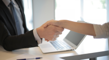 This image shows two business people shaking hands over a desk and computer.