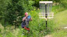 This image shows a male about to throw his frisbee into the disc golf basket.