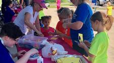 This image shows a table outdoors with kids all around learning how to make a craft at Park It.