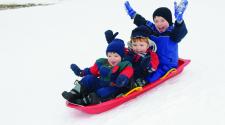 This image shows three boys on one sled sledding down the hill together.